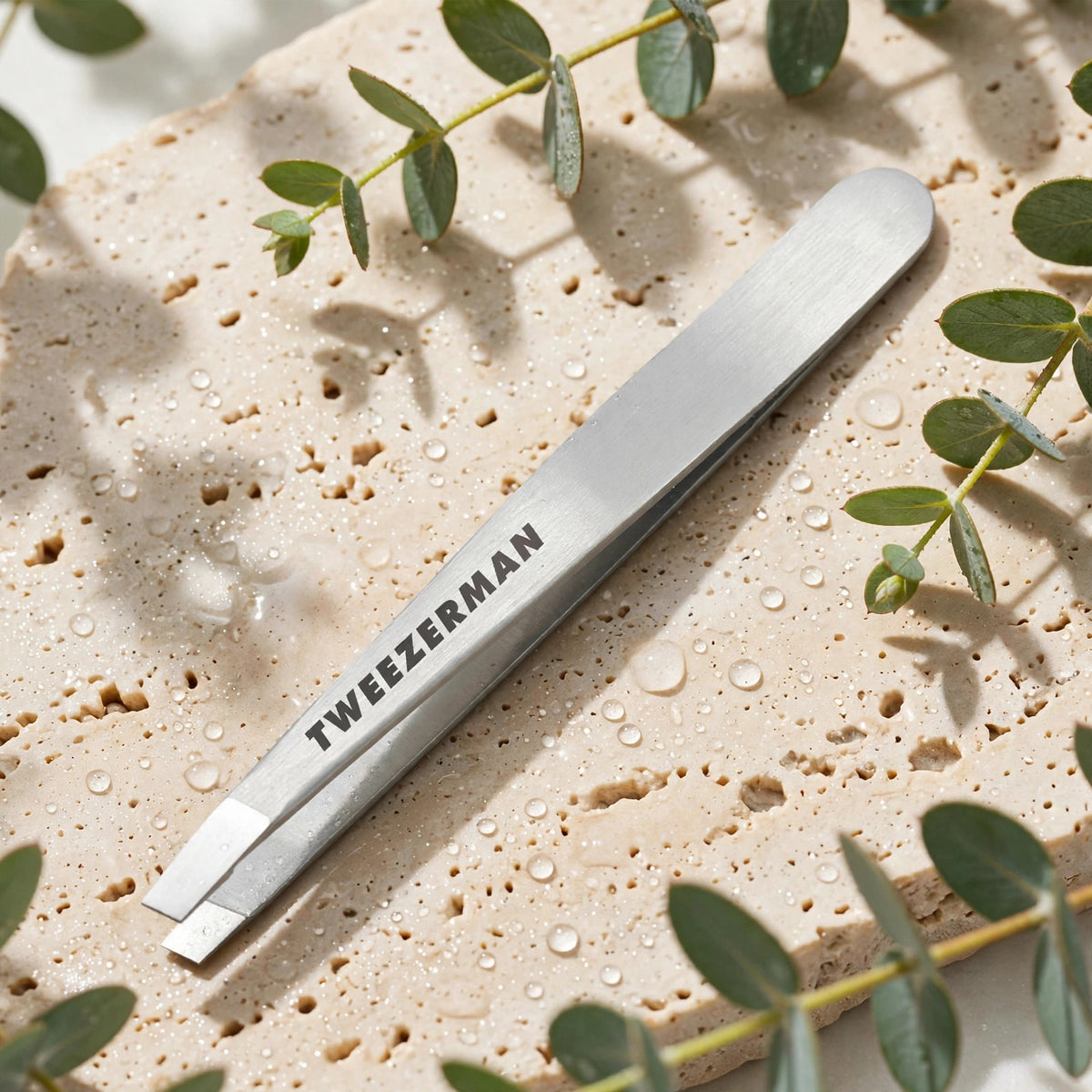 Tweezerman Classic Stainless Steel Slant Tweezer — product on travertine stone with eucalyptus